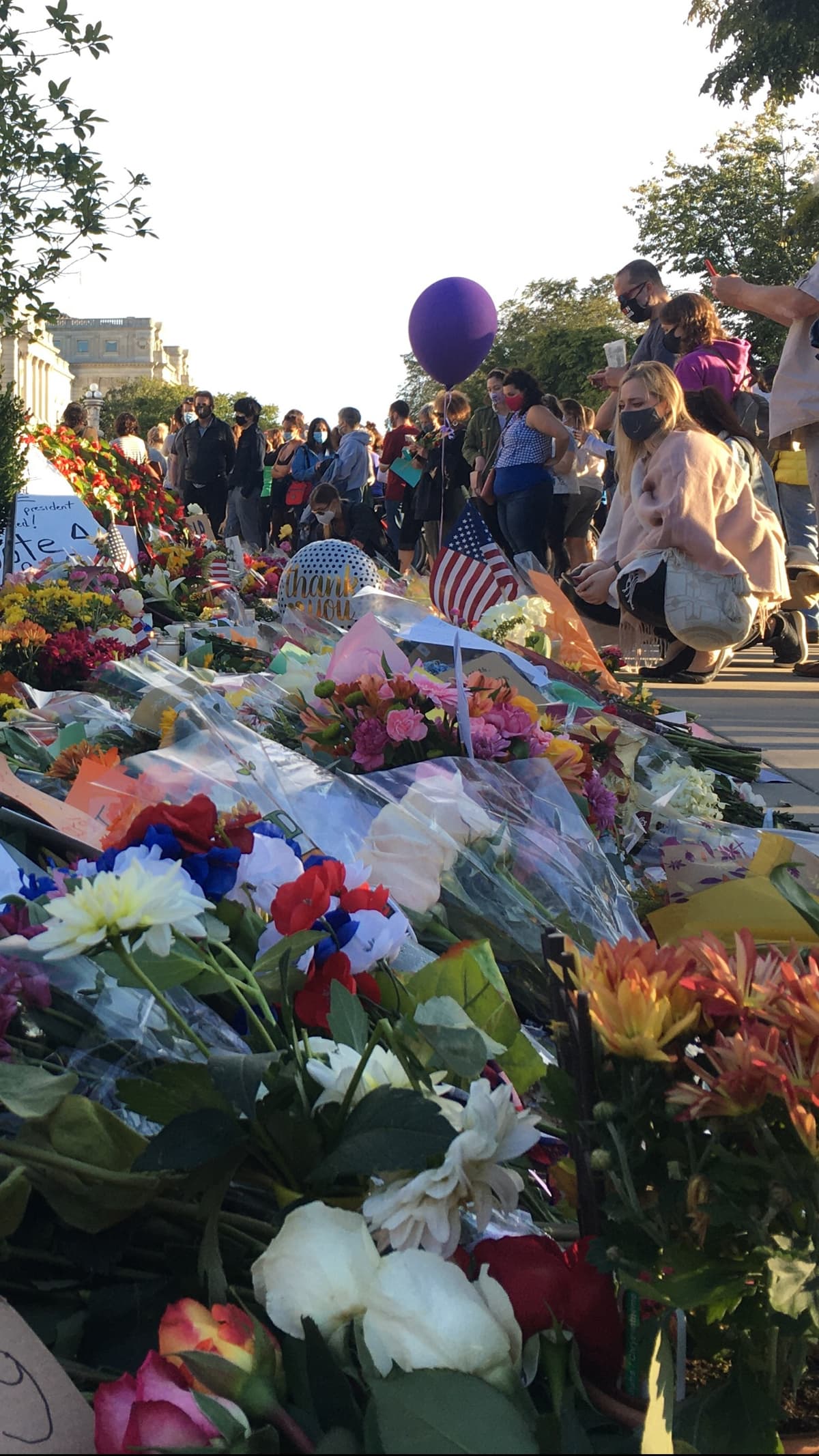 A woman in a mask looks at flowers gathered outside the U.S. Supreme Court in honor of Justice Ruth Bader Ginsburg